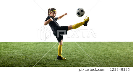 Child, girl in black uniform playing soccer, training, kicking ball with outstretched leg while standing on grassy surface against white background Child, girl in black uniform playing soccer, training, kicking ball with outstretched leg while standing on grassy surface against white background 123549355