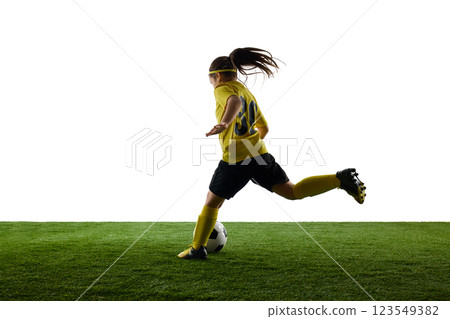 Young sportive girl, child in yellow jersey and black shorts in motion on grassy surface, dribbling ball against white studio background Young sportive girl, child in yellow jersey and black shorts in motion on grassy surface, dribbling ball against white studio background 123549382