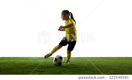 Dynamic image of child, girl in yellow jersey and black shirts in motion on grassy surface, dribbling ball against white studio background 123549391