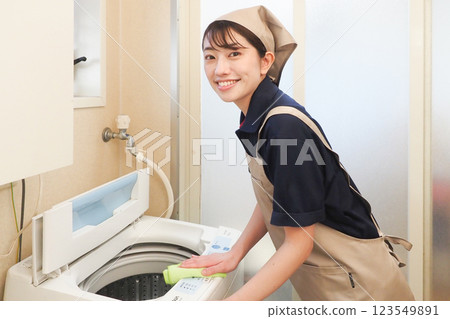 A female housecleaning worker wiping a washing machine 123549891