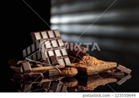 Broken bitter chocolate bars and wooden dish with cocoa powder. Broken bitter chocolate bars and wooden dish with cocoa powder. 123550644