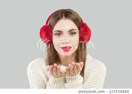 Cute woman wearing red fluffy ear muffs blowing kiss, fashion beauty portrait 123550884