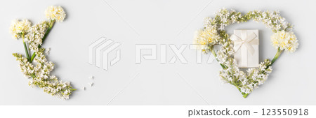 Romantic composition in the shape of a heart of white lilac flowers, white daffodils and gift box with satin bow on gray background. Holiday greeting card, an invitation to celebration. Flat lay, copy Romantic composition in the shape of a heart of white lilac flowers, white daffodils and gift box with satin bow on gray background. Holiday greeting card, an invitation to celebration. Flat lay, copy 123550918