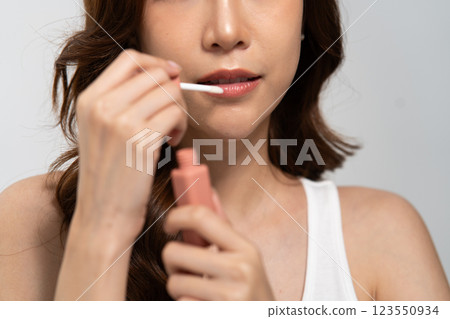Beauty routine of an Asian woman applying lip gloss for a flawless look during a skincare session 123550934