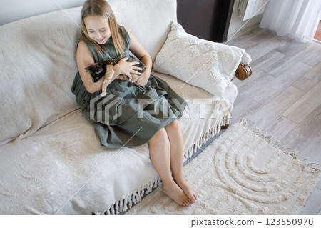 Happy little girl with cat sitting on sofa indoor 123550970