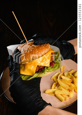 Hands in black gloves holding burger on dark background. 123551581