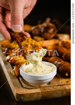 Chicken wing dipped in creamy garlic sauce close-up. Chicken wing dipped in creamy garlic sauce close-up. 123551589