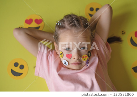 A confused, confused, awkward girl with a variety of icons and emoticons on cheeks. The concept of the problem of the influence of networks and social media on the psychology and behavior of children A confused, confused, awkward girl with a variety of icons and emoticons on cheeks. The concept of the problem of the influence of networks and social media on the psychology and behavior of children 123551800