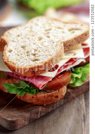 Whole grain bread sandwich with cured ham, Kumato tomato, Swiss cheese and fresh lettuce on a wooden board Whole grain bread sandwich with cured ham, Kumato tomato, Swiss cheese and fresh lettuce on a wooden board 123552082