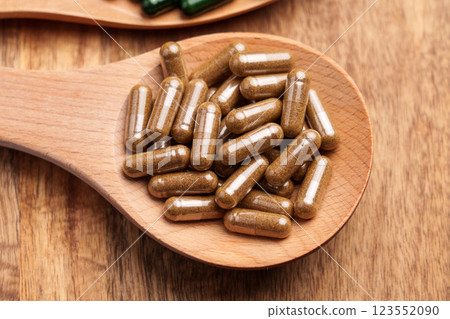 Brown herbal capsules in wooden spoon on rustic board. Natural plant-based remedies. Close-up shot. Top view 123552090