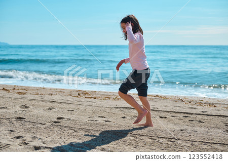 Girl Joyfully Playing by the Ocean Shore on a Sunny Day Girl Joyfully Playing by the Ocean Shore on a Sunny Day 123552418