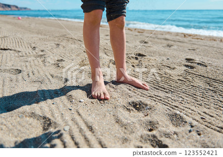 Barefoot Child Standing on a Sunlit Beach with Ocean View 123552421
