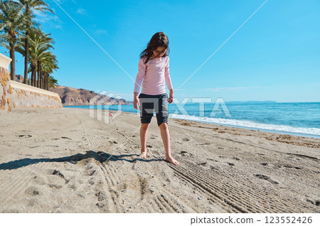 Young Girl Playing on a Sunny Beach with Clear Blue Skies Young Girl Playing on a Sunny Beach with Clear Blue Skies 123552426