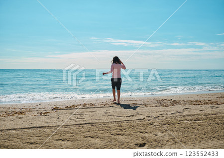 Young Woman Strolling on a Serene Beach Under Clear Blue Skies Young Woman Strolling on a Serene Beach Under Clear Blue Skies 123552433