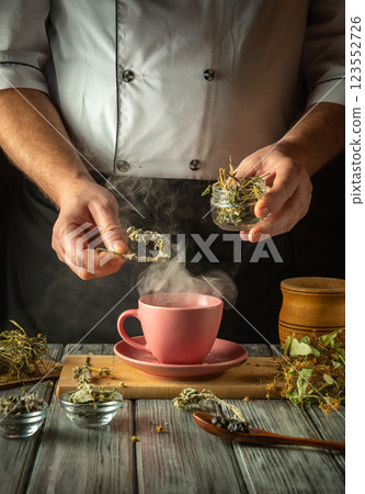 A skilled hands carefully add dried herbs to a steaming pink cup, creating a soothing herbal infusion. The warm kitchen radiates comfort as nature aromas fill the air, inviting tranquility 123552726