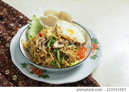 Fried noodles on a round white plate with a brown patterned cloth on a white marble table, Indonesian food, negative space Fried noodles on a round white plate with a brown patterned cloth on a white marble table, Indonesian food, negative space 123553267