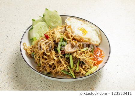 Fried mei with round egg topping, cucumber slices, sauce, white marble texture table background, indonesian food 123553411