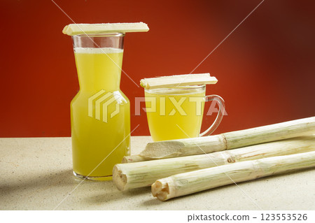 two glasses of sugarcane juice and topping of sugarcane slices in the glass, sugarcane juice with sugarcane stalks on white marble table, orange background 123553526