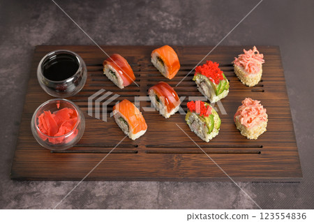 Set of sushi roll with rice and fish, soy sauce and ginger into a glass bowl on wooden serving board. Dark black texture background with copy space. Japan menu. Asian food 123554836