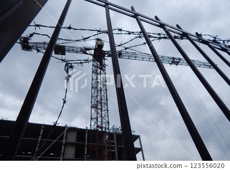 Unfinished construction site fenced with barbed wire and a blurred construction crane in the background Unfinished construction site fenced with barbed wire and a blurred construction crane in the background 123556020