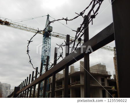 Stopped high-rise construction crane behind a metal fence with barbed wire in focus on foreground Stopped high-rise construction crane behind a metal fence with barbed wire in focus on foreground 123556022