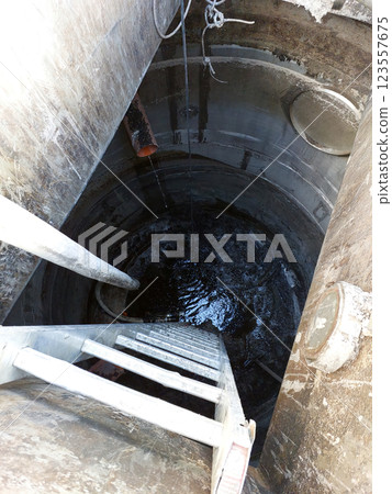 Exploring the Depths of an Urban Sewer Well With a Ladder Leading Into Darkness 123557675