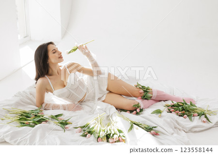Elegant woman in white lingerie lying on bed with tulips, enjoying flowers in soft natural light, romantic and feminine aesthetic 123558144