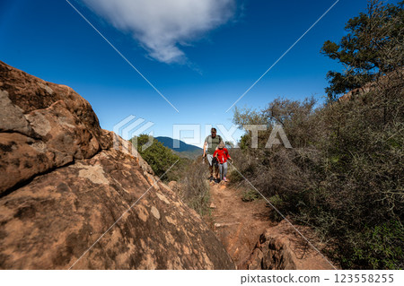 Father and daughter hiking on rugged mountain trail under clear blue sky 123558255