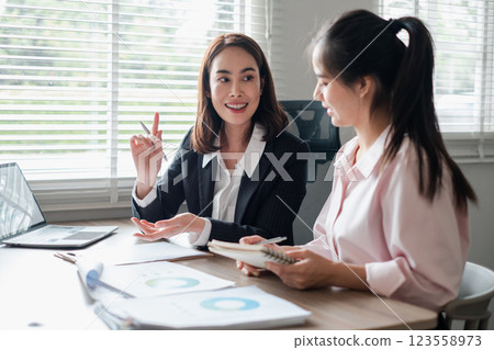 Two businesswomen engaged in a discussion over reports in a bright office environment, showcasing teamwork and collaboration. Two businesswomen engaged in a discussion over reports in a bright office environment, showcasing teamwork and collaboration. 123558973