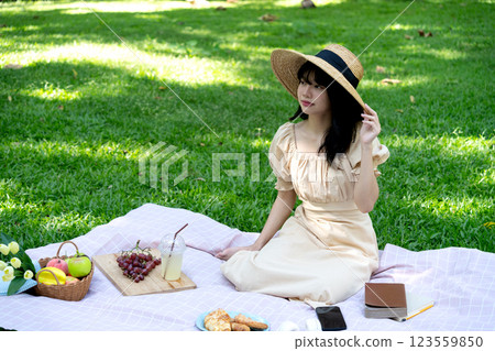 young woman is relaxing on a blanket with food book and drinks young woman is relaxing on a blanket with food book and drinks 123559850