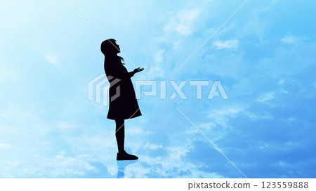 Sideways silhouette of a woman looking up with her hands raised_Blue sky background 123559888
