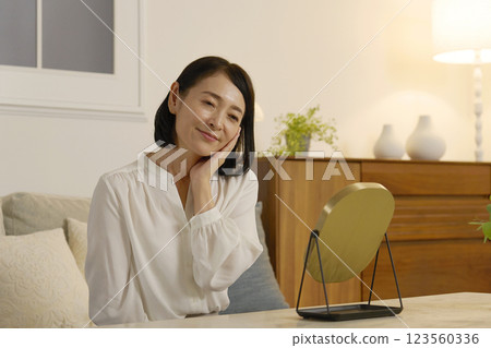 A woman in her 50s doing skin care in the living room at night A woman in her 50s doing skin care in the living room at night 123560336
