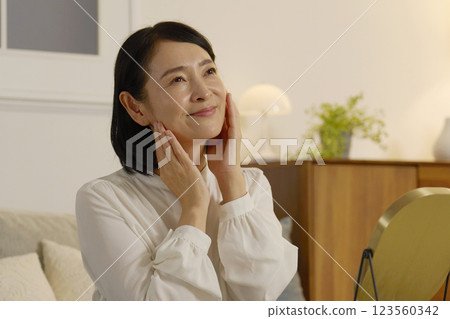 A woman in her 50s applying lotion to her face in the living room at night A woman in her 50s applying lotion to her face in the living room at night 123560342