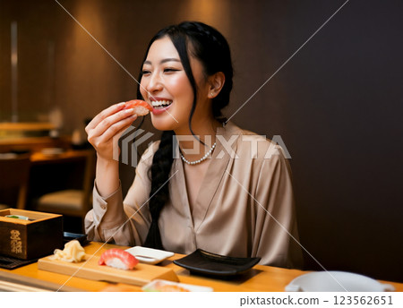 A smiling woman eating nigiri sushi A smiling woman eating nigiri sushi 123562651