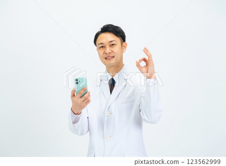 A middle-aged male doctor/researcher wearing a white coat holding a smartphone and showing a check mark 123562999