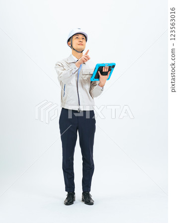 Full-body photo of a middle-aged man wearing work clothes inspecting a tablet 123563016