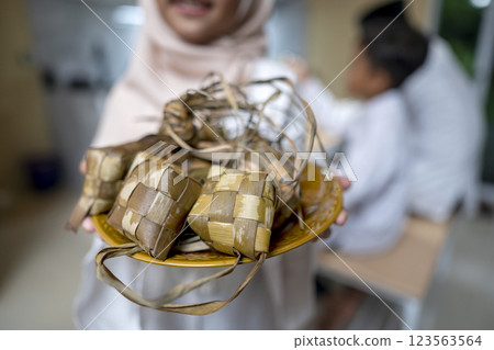 A Muslim girl serving ketupat rice dumpling on the plate for her family. Traditional Muslim food during the celebration of Eid Al Fitr, Idul Fitri, and Ramadan Mubarak celebration 123563564