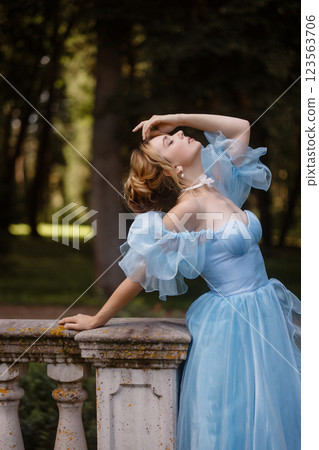 Romantic Woman in a Light Blue Gown Posing on a stone balustrade in a picturesque garden. 123563706
