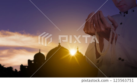 Muslim man praying with prayer beads with a view of the silhouette of the mosque with sunlight in the sunset scene background. Concept of Religion, Spiritual or Ramadan Muslim man praying with prayer beads with a view of the silhouette of the mosque with sunlight in the sunset scene background. Concept of Religion, Spiritual or Ramadan 123563751