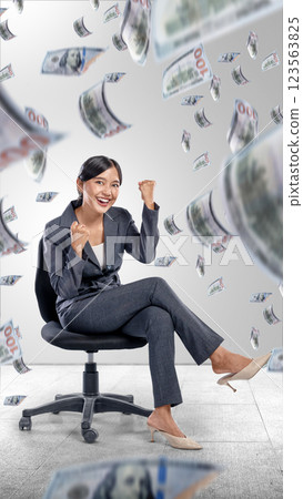 Asian Indonesian businesswoman sitting on the office chair with an excited expression and a rain of money. Concept of business, finance, and economy Asian Indonesian businesswoman sitting on the office chair with an excited expression and a rain of money. Concept of business, finance, and economy 123563825
