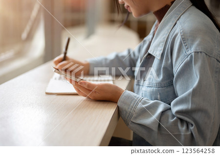 A person is holding smartphone while noting down or writing down in the notebook. A person is holding smartphone while noting down or writing down in the notebook. 123564258