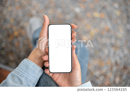 A close up shot of the pair of hand holding white screen smartphone while sitting cross legged. A close up shot of the pair of hand holding white screen smartphone while sitting cross legged. 123564285