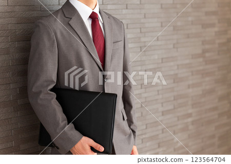 A middle-aged male businessman wearing a gray suit leaning against a wall 123564704