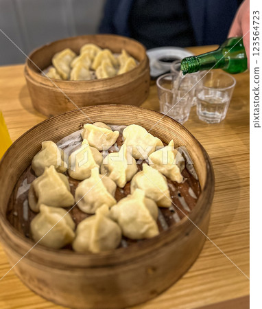 Steamed dumplings in in wooden bamboo steamer like a plate with a glass of juice and bottle of soju at the restaurant 123564723