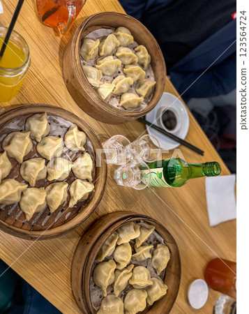 Steamed dumplings in in wooden bamboo steamer like a plate with a glass of juice and bottle of soju at the restaurant Steamed dumplings in in wooden bamboo steamer like a plate with a glass of juice and bottle of soju at the restaurant 123564724