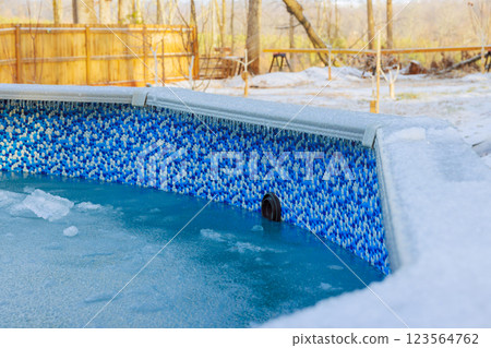 Winter landscape features frozen pool with ice formations, surrounded by trees wooden fence 123564762