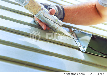 Contractor is sealing metal siding with caulk gun in home renovation project under construction 123564764