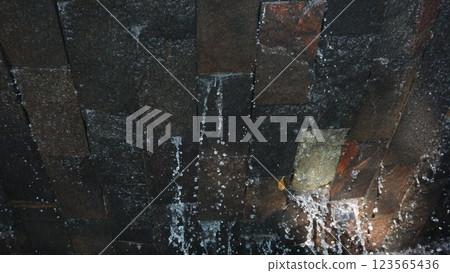 Water Cascading Over Textured Stone Wall 123565436