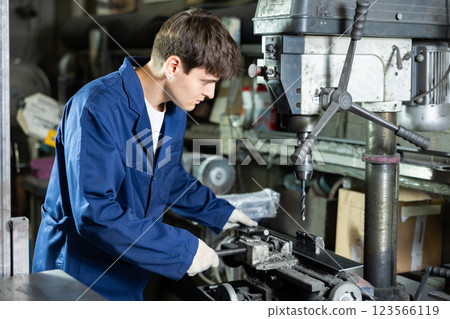 Guy worker at metallurgical plant drills hole in metal plate using drilling machine Guy worker at metallurgical plant drills hole in metal plate using drilling machine 123566119
