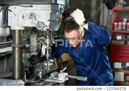 Experienced machinist using drill press in industrial metal workshop 123566278